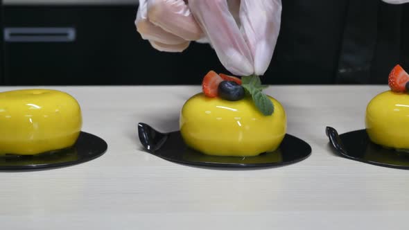 the Hands of the Pastry Chef in Gloves Decorate the Yellow Cakes with Berries