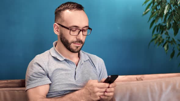 Smiling Man Texting Using Mobile Sit on Comfy Sofa in Weekend
