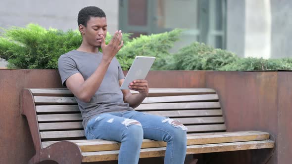 Young African Man Having Loss on Tablet on Bench