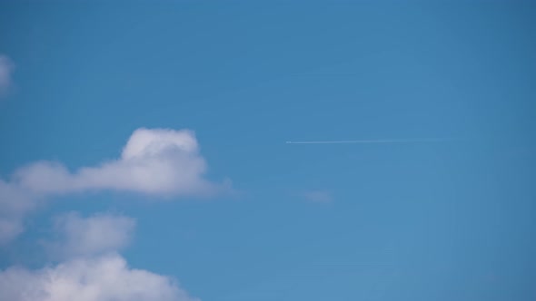 Distant Passenger Jet Plane Flying on High Altitude on Blue Sky with White Clouds Leaving Smoke