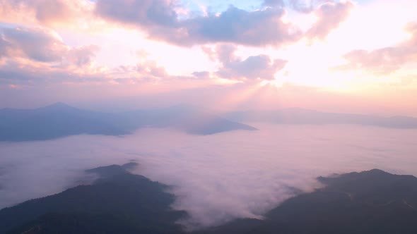 The rays of the sun shine through the clouds into the misty sea above the mountains in the morning