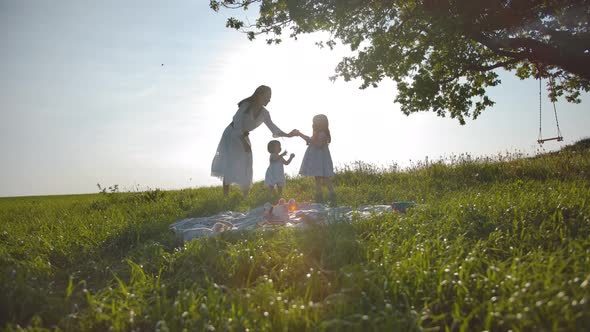 Happy Family of Mom and Two Little Daughters Are Resting in a Meadow, Far From the City.