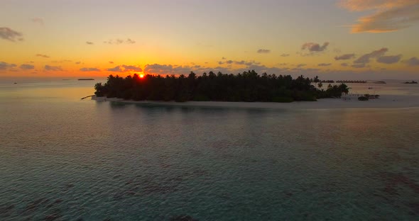 Aerial drone view of a scenic tropical island in the Maldives at sunset.