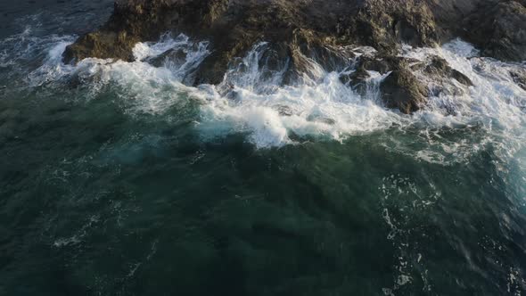 Aerial View of Waves crashing at rocky cliffs with foam and splashing in the sea