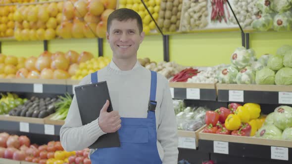 Portrait of Young Brunette Caucasian Man in Uniform Posing in Grocery Shop. Positive Employee