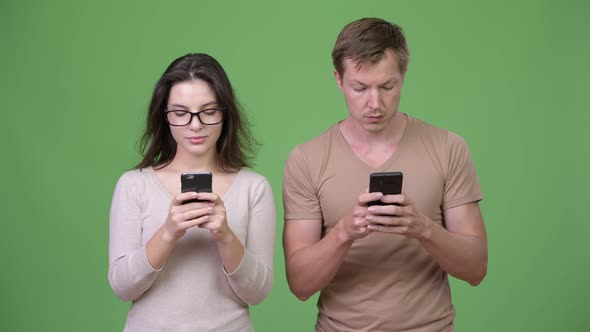 Young Couple Using Phone Together Against Green Background