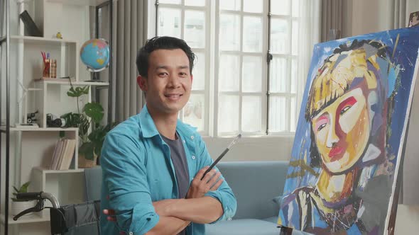 Asian Artist Man In Wheelchair Holding Paintbrush, Cross His Arms And Smile