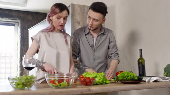 Young Couple Making Salad and Talking in Kitchen