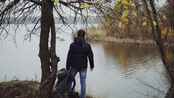 Man standing near river. Young man with backpack walking near the river in autumn season