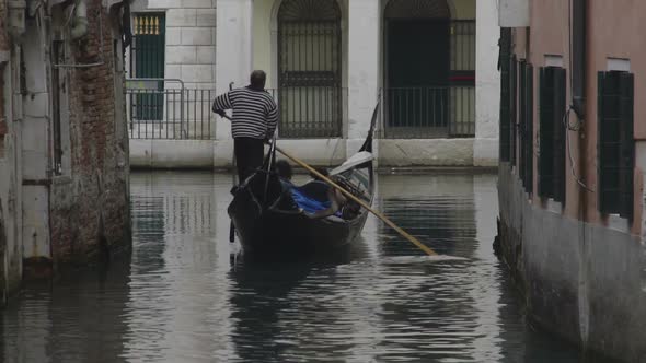 Gondolier with Passengers Onboard Rowing Along Narrow Water Passage, Back View