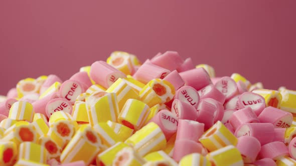 Colored Striped Caramel Candies with the Inscription Love Rotating on a Pink Background