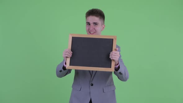Happy Young Businessman Holding Blackboard and Looking Surprised
