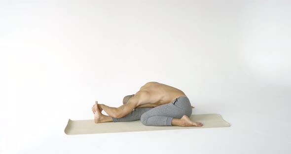 Muscular Male Yogi Doing Leg Stretching. He Stretches Each Leg in Turn. White Background