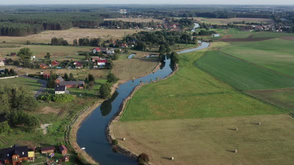 Aerial countryside shot of a farming village by the river among farms and fields and forests.