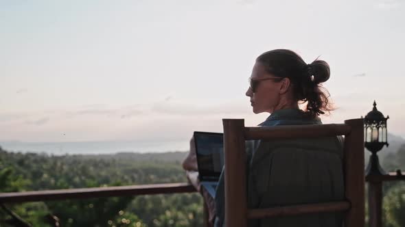 Freelancer woman sits with a laptop on a high bar chair. 