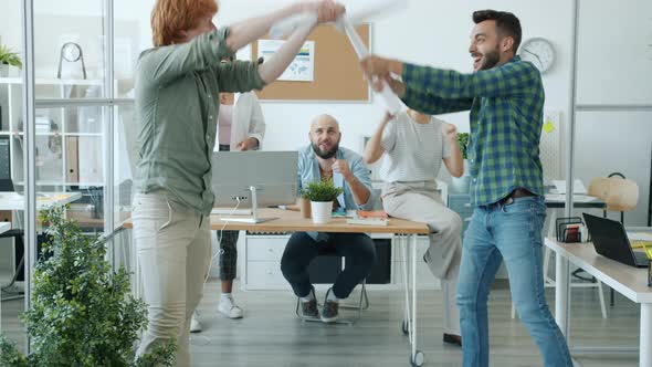 Playful Men Office Workers Fighting Paper Swords Enjoying Funny Activity Relaxing at Work