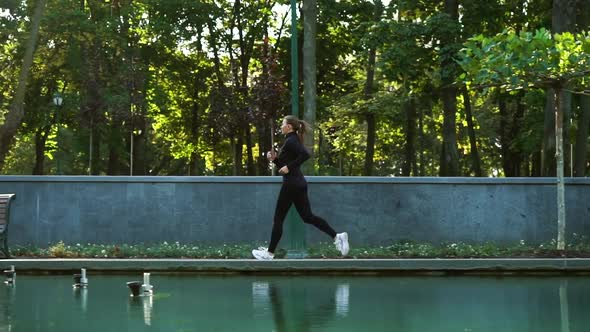 Woman running along pond in park with fountain