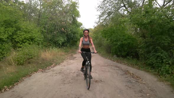 Aerial Slow Motion Shot of Young Sport Woman Rides Bicycle on Countryside Dusty Road at Summer