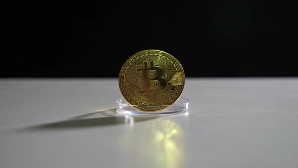 Golden Bitcoin on a Stand Illuminated and Reflects Light on a White Table