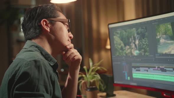 Asian Male Video Editor Thinking While Works With Footage And Sound On His Personal Computer