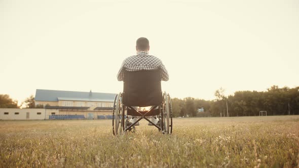 Disabled Man in Wheelchair Stands in Middle of Field Enjoying Beauty of Nature and Raises His Hands