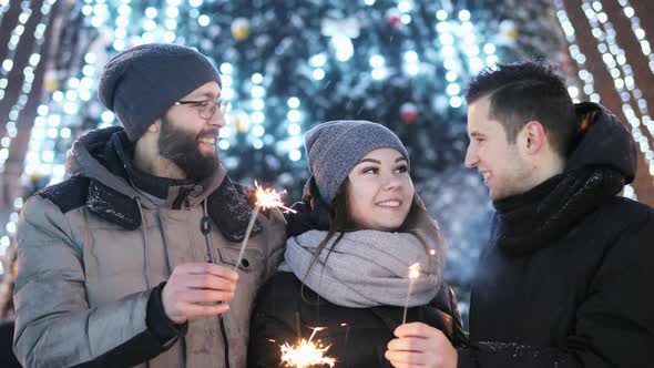 Friends Celebrating New Year Outdoors, Keeps Sparklers, Lights in the Blur in the Background