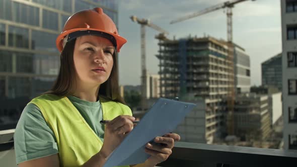 Young Female Builder in a Signal Vest and Helmet Writes Something