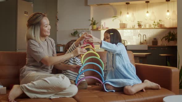 Young Asian Mother and Little Siblings Spend Time at Modern Flat Play Together Seated on Sofa Enjoy