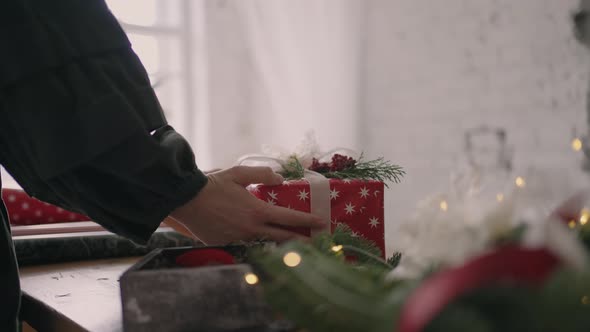 A Young Woman Decorating a Gift on a Wooden Table with Garlands Turns Over and Puts on the Table a