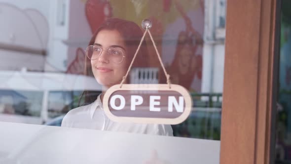 Happy small business girl changing closed to open sign on window smiling