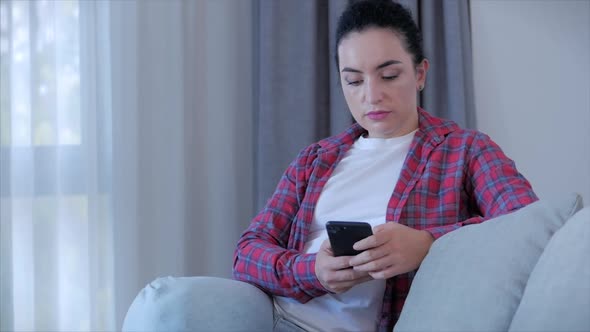 Young Serious Woman Working Freelancer Typing on Phone Sitting on Sofa at Home, Businesswoman Sits