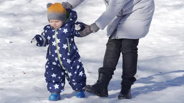 Kid Takes the First Steps in the Snow Walking with Mom