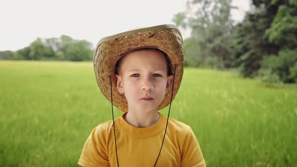Kid in a straw hat is eating a big red apple. Portrait of a boy on a warm sunny day