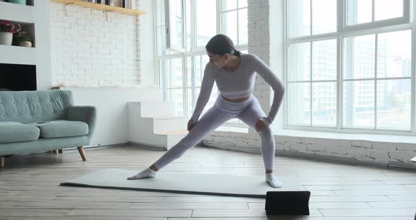 Athletic Young Woman Stretches Legs and Arms at Home with Large Windows in Morning