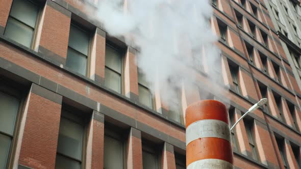 Steam Comes From the Striped Pipe, Against the Background of Tall Brick Buildings