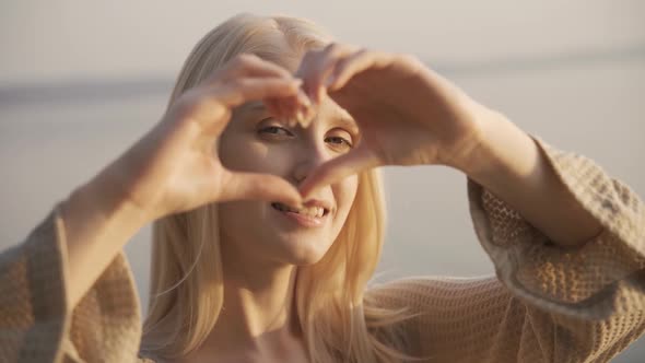 Young Beautiful Woman Shows a Heart with Her Hands Smiles and Looks at the Camera