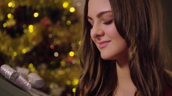 A Young Beautiful Woman Sits in a Cozy Living Room and Examines a Gift Box - Closeup