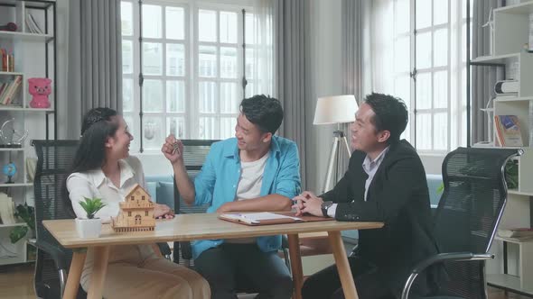 Asian Man Sitting With A Woman Receiving The Keys From A Real Estate Agent
