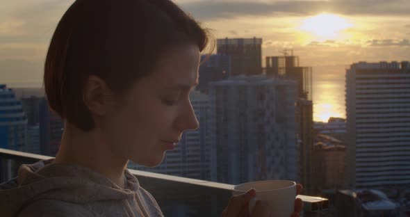 Side Portrait of Attractive Woman Drinking Hot Tea on Terrace and Enjoying Beautiful View