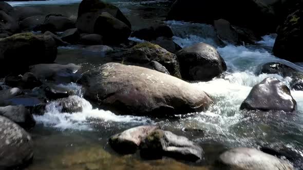 Drone footage flying close to rocks sticking out of pristine clean water below the falls in the Coqu