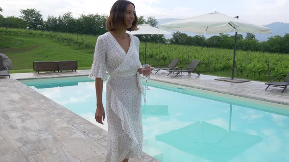 A woman walking with a glass of white wine at a pool traveling at a luxury resort in Italy, Europe.