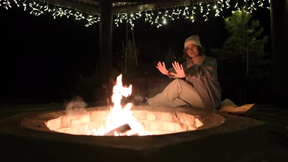 Young Woman Sits Resting By the Fire at Night Outdoors on Nature