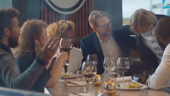 Mature Man in Safety Mask Joining Group of Diverse Friends in Modern Restaurant