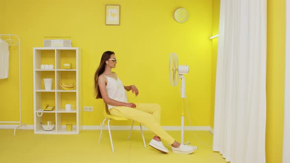 Young Woman Is Sitting In Office Chair In Front of Fan