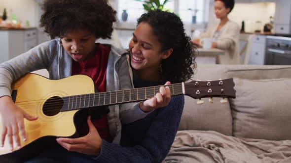 Mixed race mother and daughter sitting on couch playing guitar