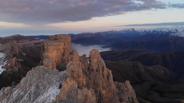 Aerial View of the Top of a Rocky Mountain with Mountain Ranges and a Lake with Low Clouds