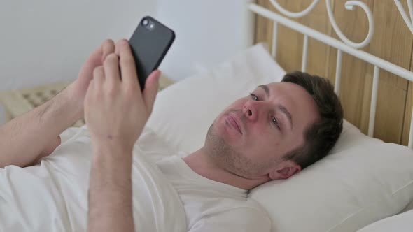 Attractive Young Man Using Smartphone in Bed 