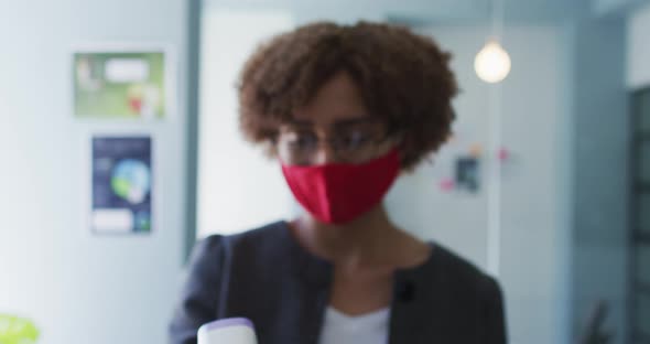 Portrait of african american woman wearing face mask holding temperature gun at modern office