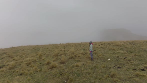 A Slender Young Woman in Travel Clothes Walks and on a High Plateau in Foggy Weather Against the
