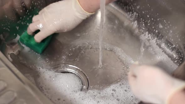 Cleaning kitchen sink with green sponge and foamed detergent